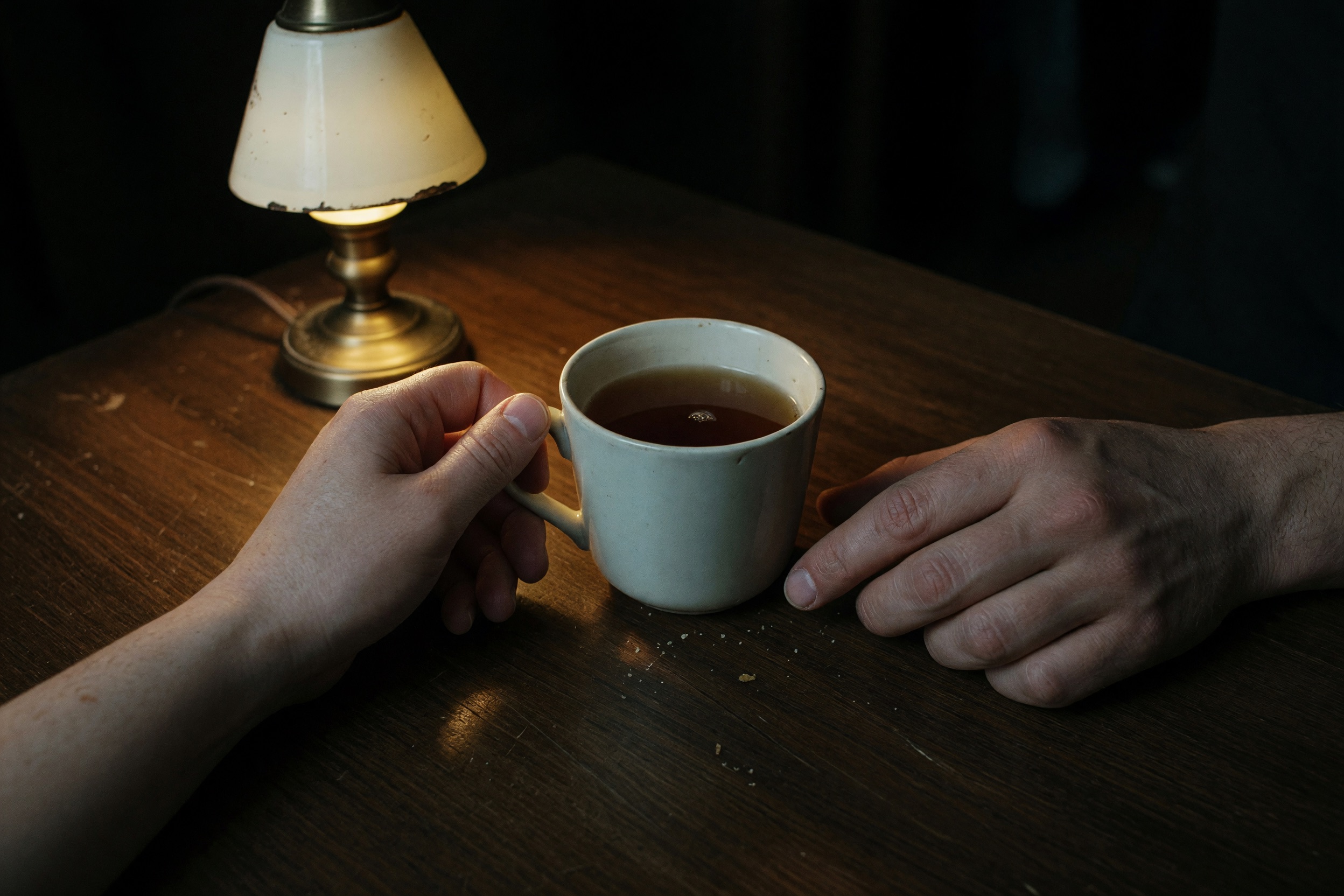 Hands and a plain cup on a table under one small lamp